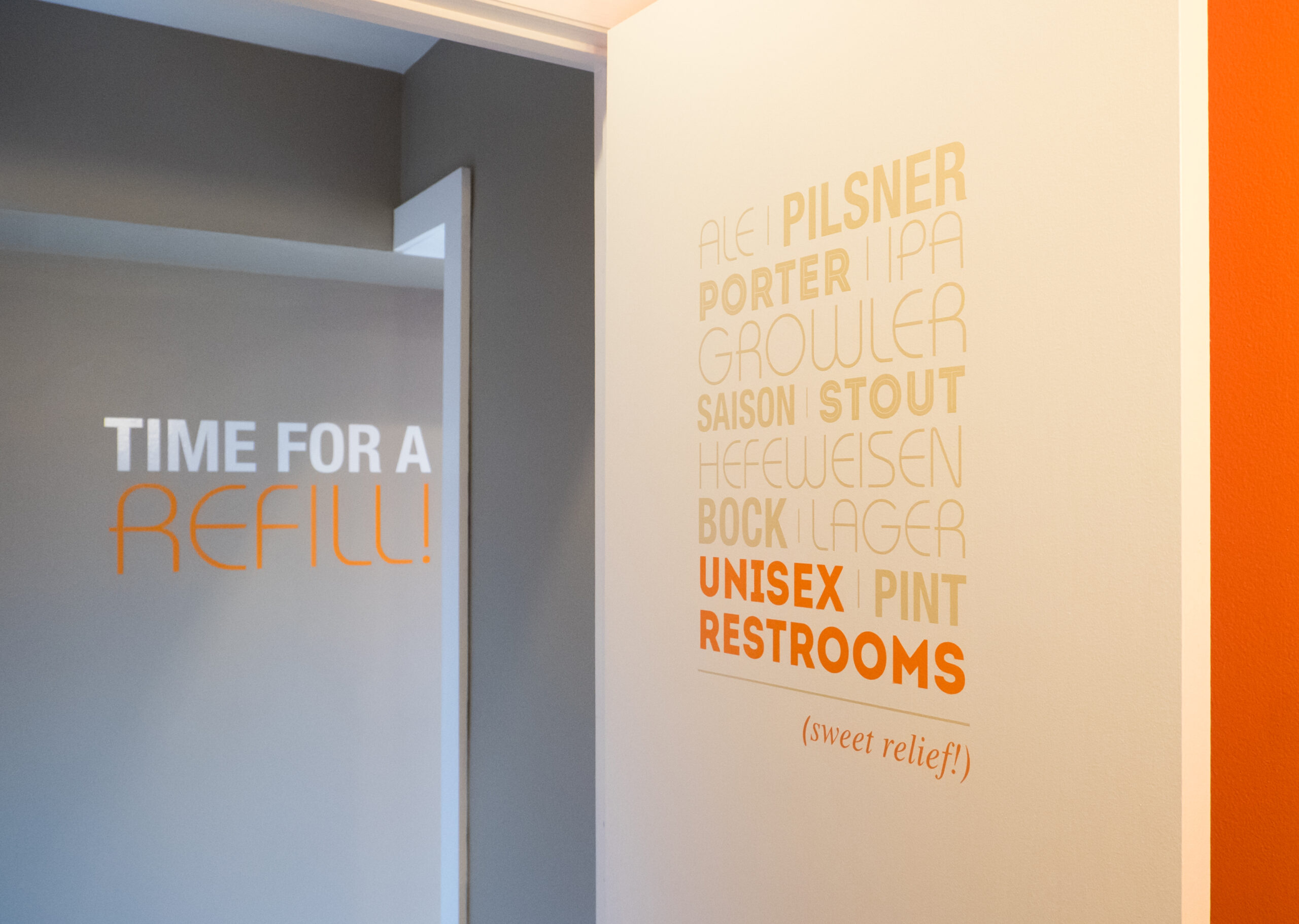 Contact page image is of two walls, a corner in our brew house. The left wall has text that reads "time for a refill!". The right wall reads Ale, Pilsner, Porter, IPA, Growler, session, stout, Hefewiesen, Bock, Larger, Pint all in dark cream font. In bright orange font Unisex Restrooms.
