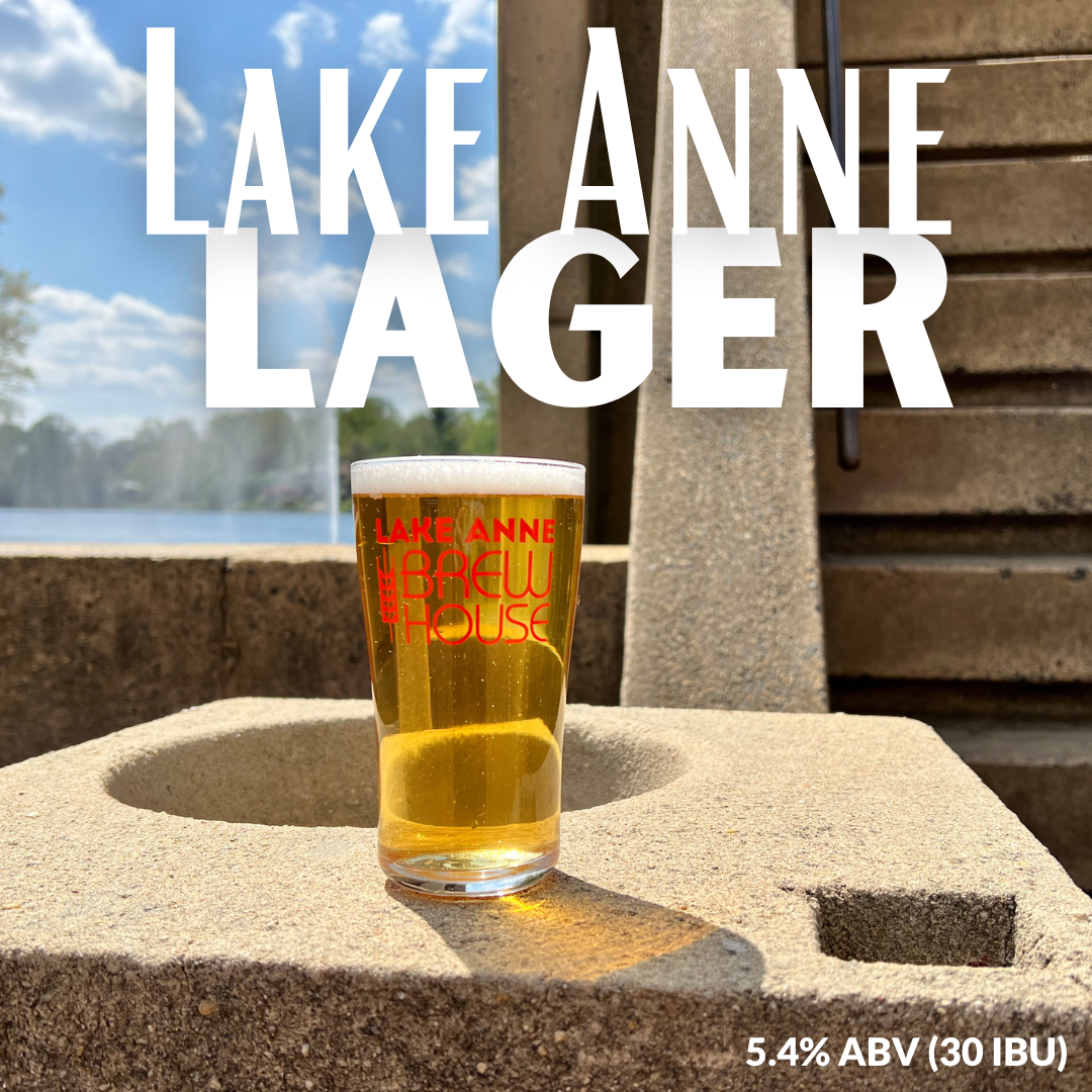 Lake Anne Lager Image is our small batch crafted lager on a cemeent table with a lake and forest in the background.